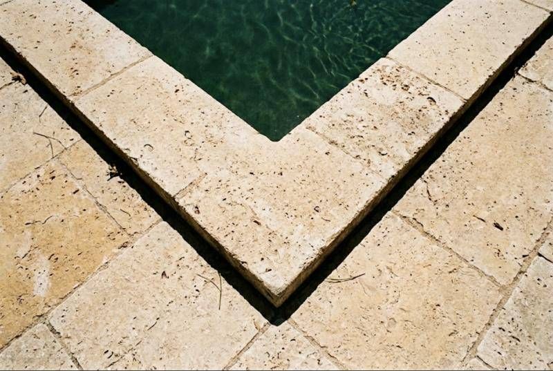 Angle de margelle et plage en travertin vieilli beige, alvéoles naturelles visibles